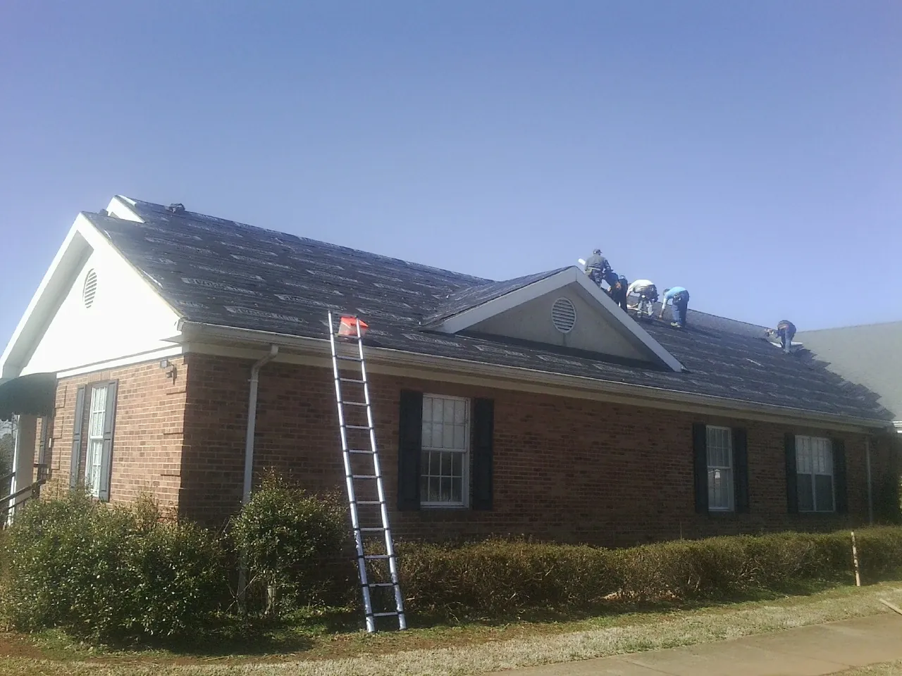 Crew tearing shingles off a brick ranch roof with a ladder set — Emergency Roof Repair work by our crew in Warner Robins