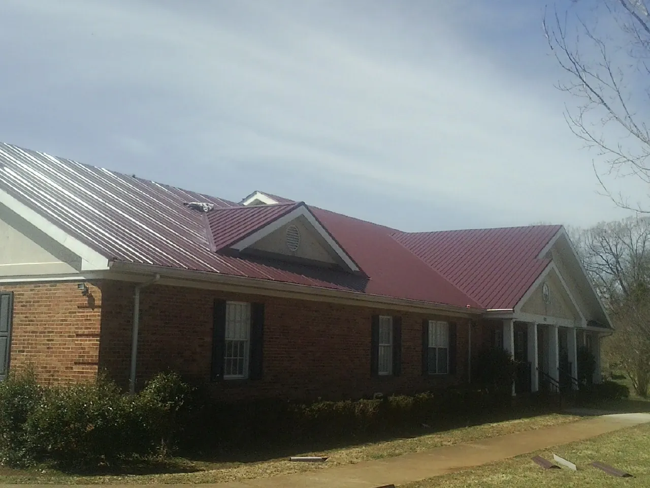 Red metal roof with gabled entries on a long brick building, from a Hail Damage Roof Repair job in Warner Robins