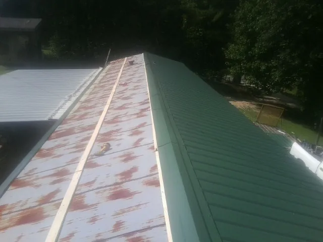 Old rusted panels beside newly installed green metal roofing — Wind Damage Roof Repair by Roofing Brothers in Warner Robins