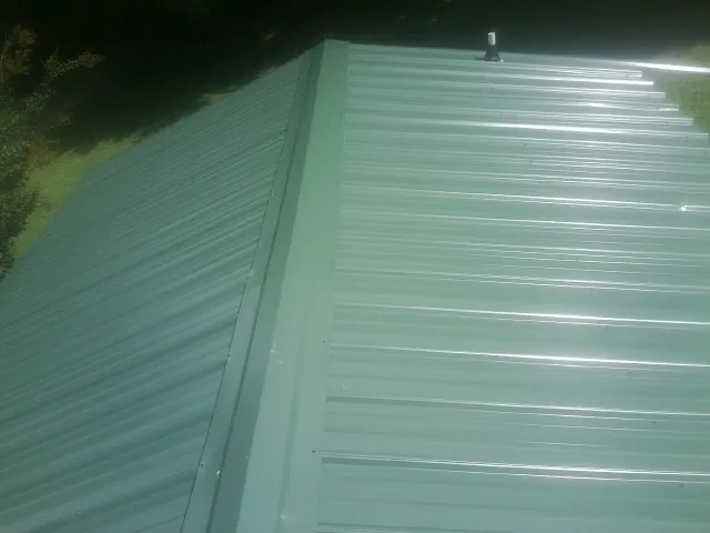 New green metal panels meeting at the ridge of a roof — Flat Roof Repair work by our crew in Warner Robins