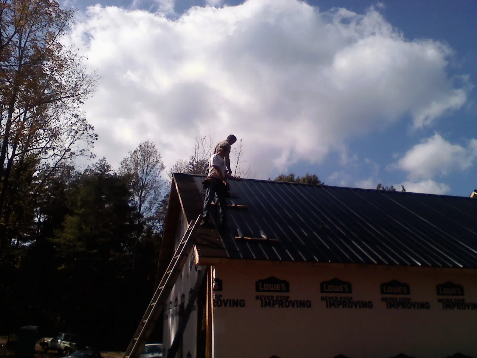 Roofer fastening dark metal panels high against a cloudy sky, from a Roof Inspection job in Warner Robins