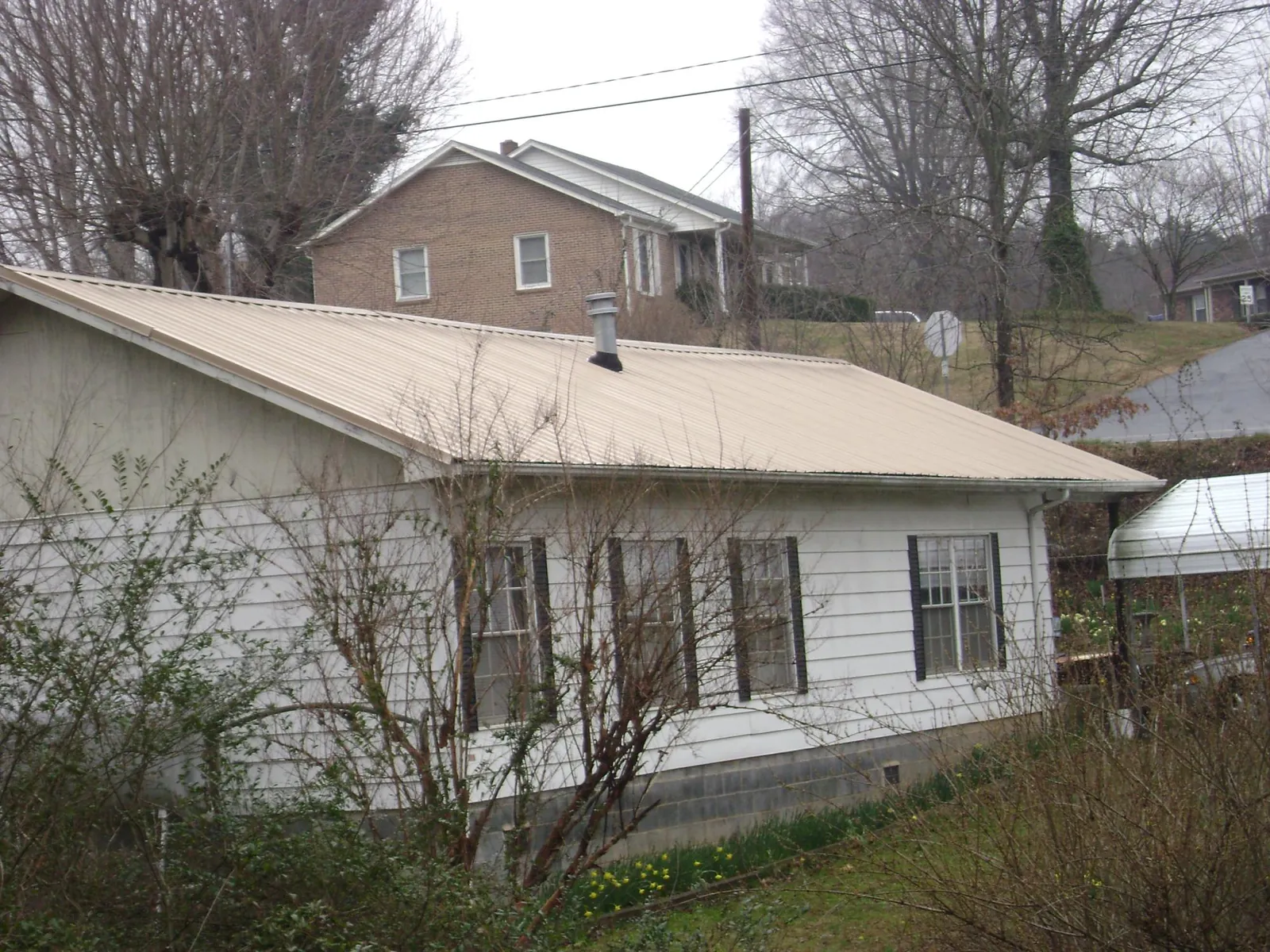 Tan metal roof on a white sided house set into a hillside — Commercial Roofing by Roofing Brothers in Warner Robins
